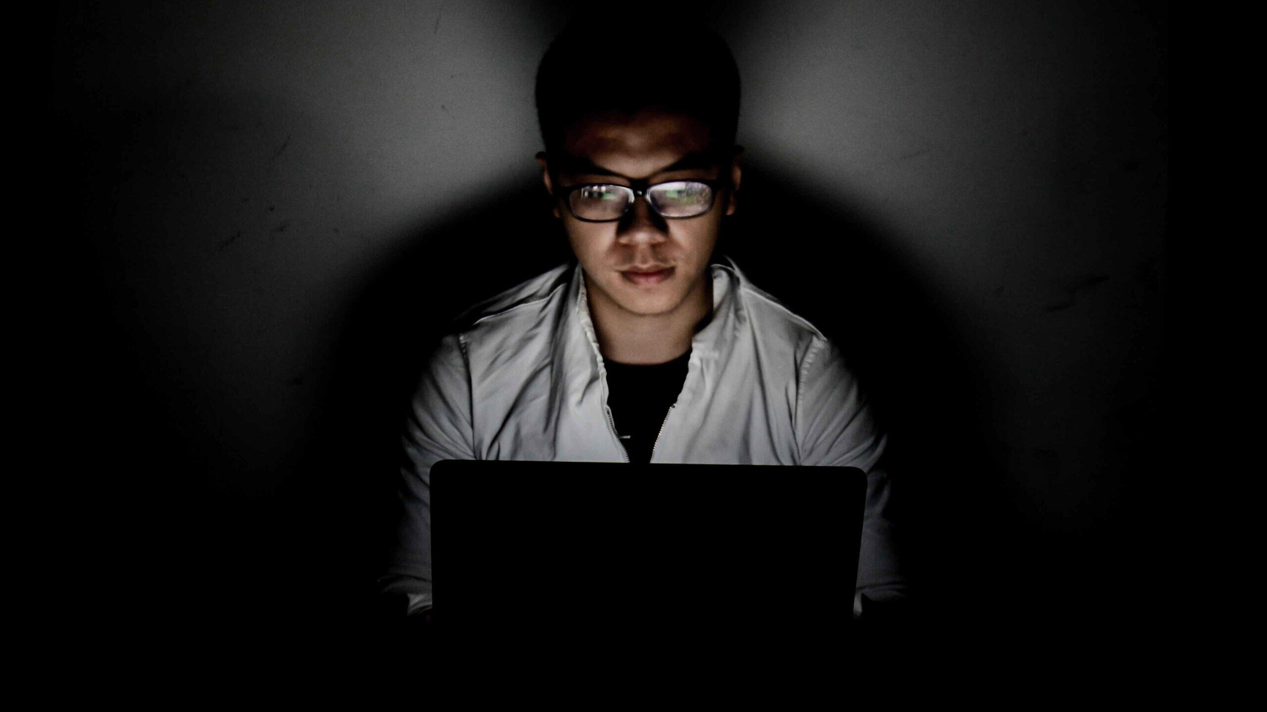 Male student watching a computer in the dark