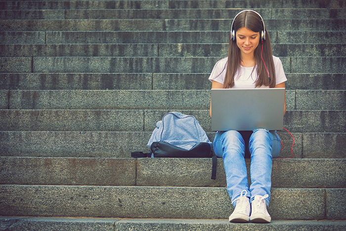 Woman sitting on stairs and working on a computer with headphones