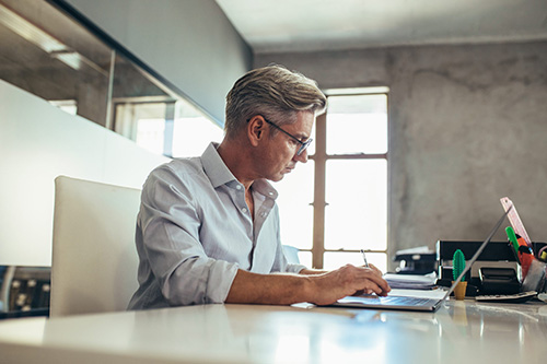 Man with glasses sitting at a table working on a computer