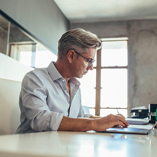 Man with glasses sitting at a table working on a computer